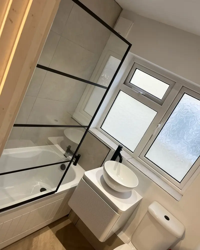 A renovated bathroom in Wickford with a black-framed bath screen, light tiles and a white vanity